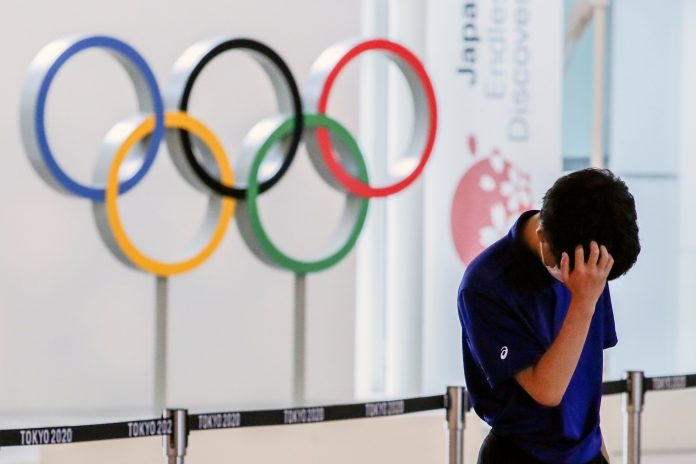 A staff standing in front of Olympic rings reacts while waiting for the arrival of foreign athletes at Haneda Airport ahead of Tokyo 2020 Olympic Games, in Tokyo