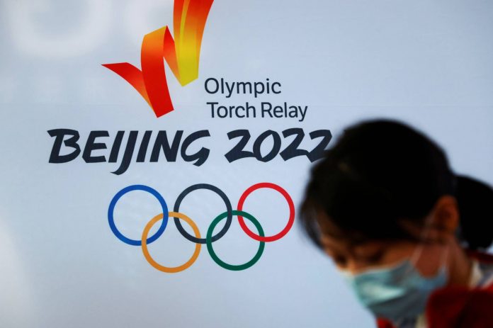 A woman stands in front of the logo of the Beijing 2022 Winter Olympics before the Olympics flame exhibition tour at Beijing University of Posts and Telecommunications, China