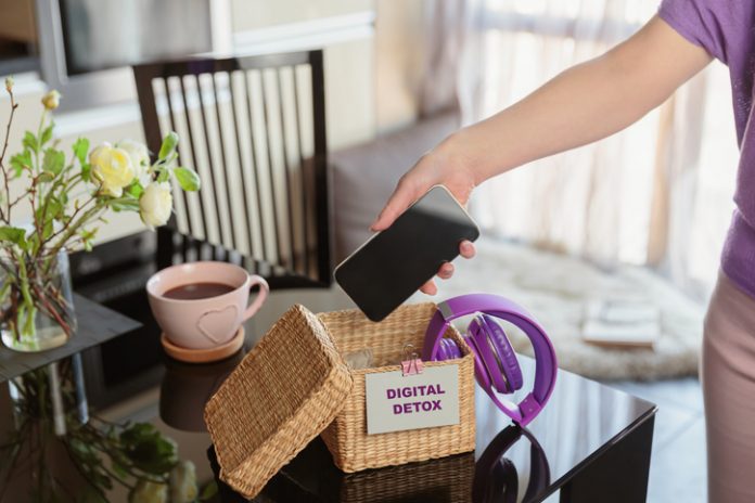 Woman putting phone into box with different gadgets at home